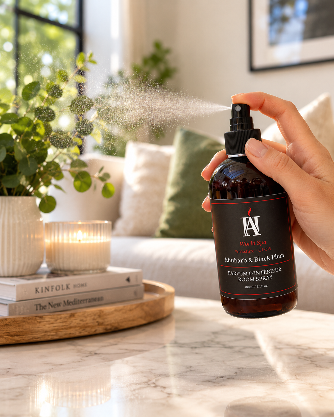 AromaHoliday Glow Rhubarb & Black Plum room spray being sprayed in a luxury living room, creating a warm and inviting home fragrance experience.